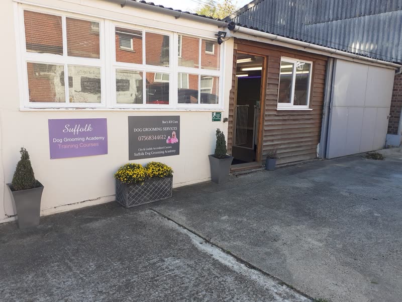 The grooming salon from the forecourt, a cream single-storey building with clipped bay trees either side of the open doorway
